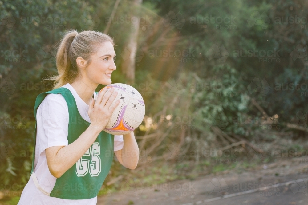 side view shot of a young woman in sports wear holding a net ball with two hands on a sunny day - Australian Stock Image
