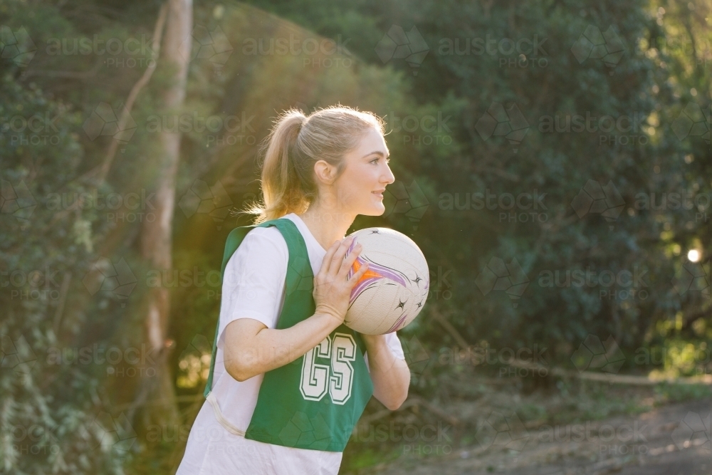 side view shot of a young woman in sports wear holding a net ball with two hands on a sunny day - Australian Stock Image