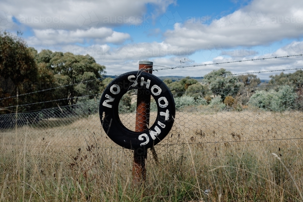 Sign made from old black tyre tied to a rusted post with a white painted message "NO SHOOTING" - Australian Stock Image