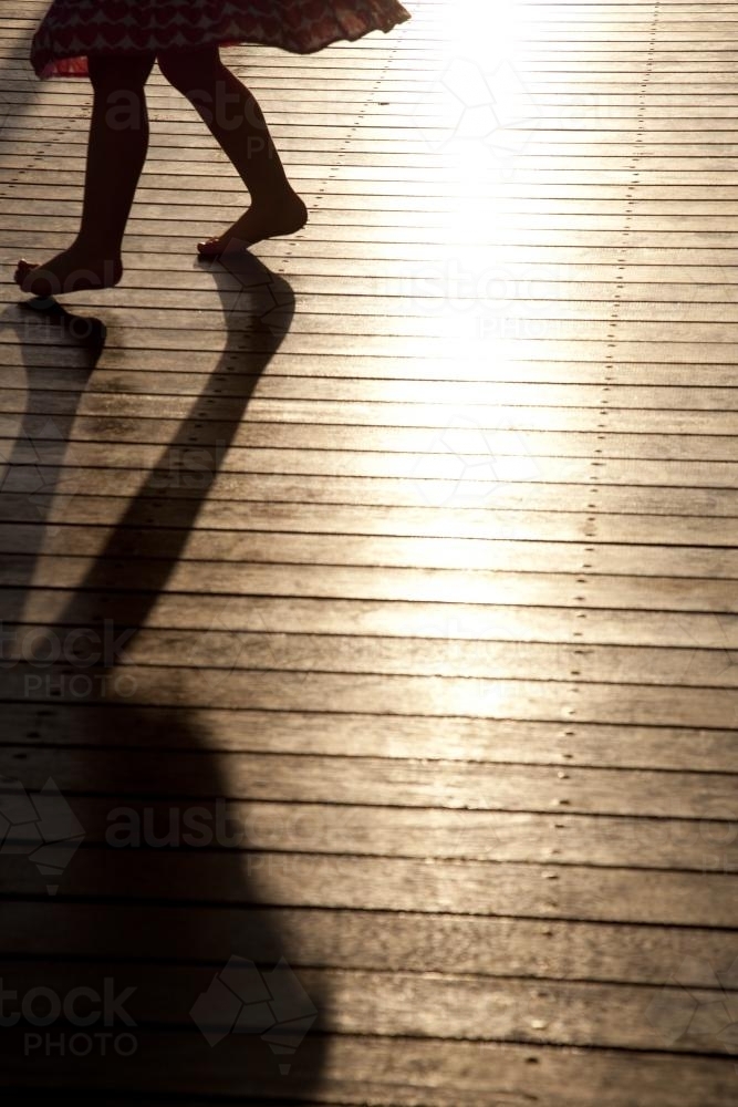 Silhouette and shadow of a young girl dancing on a sunlit deck - Australian Stock Image