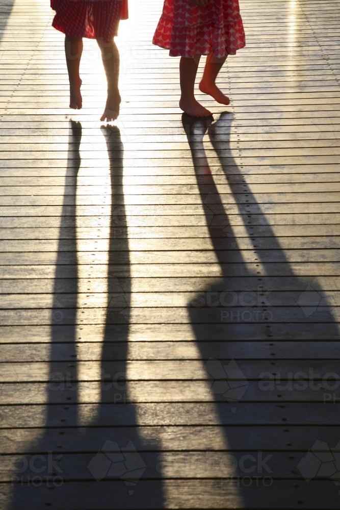 Silhouette and shadows of two young girls standing on a deck - Australian Stock Image