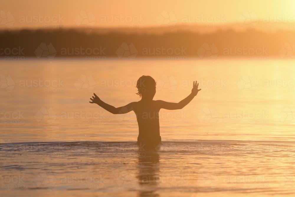 Silhouette of a child in water at sunset - Australian Stock Image