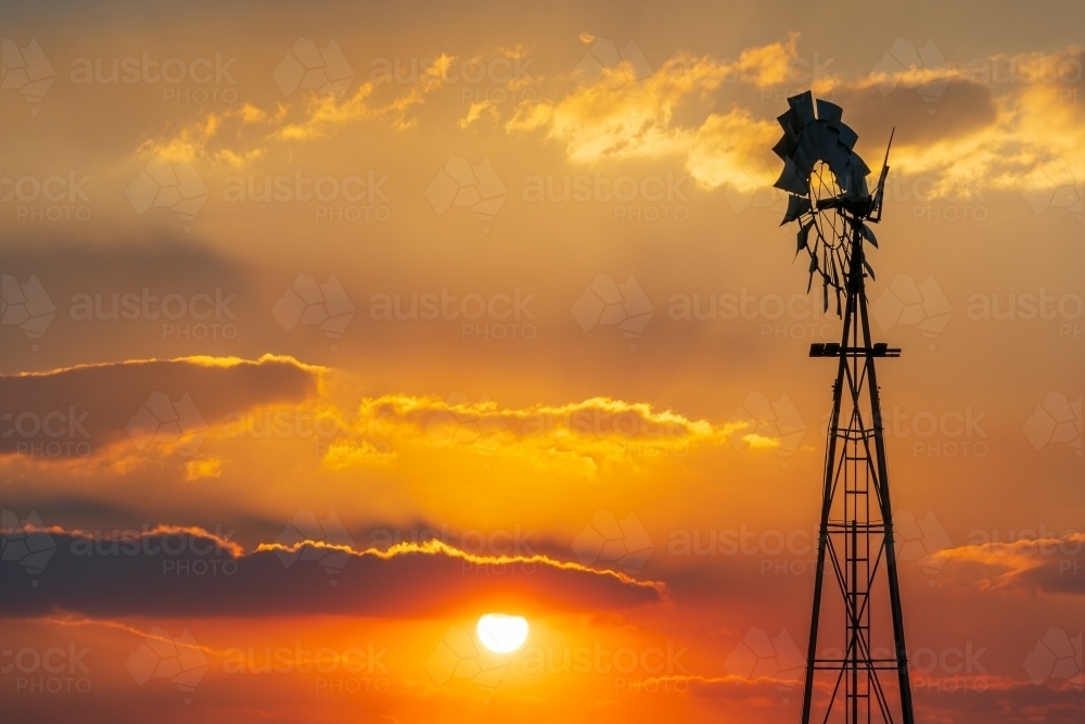 Silhouette of a farm windmill against a smokey sunset sky - Australian Stock Image