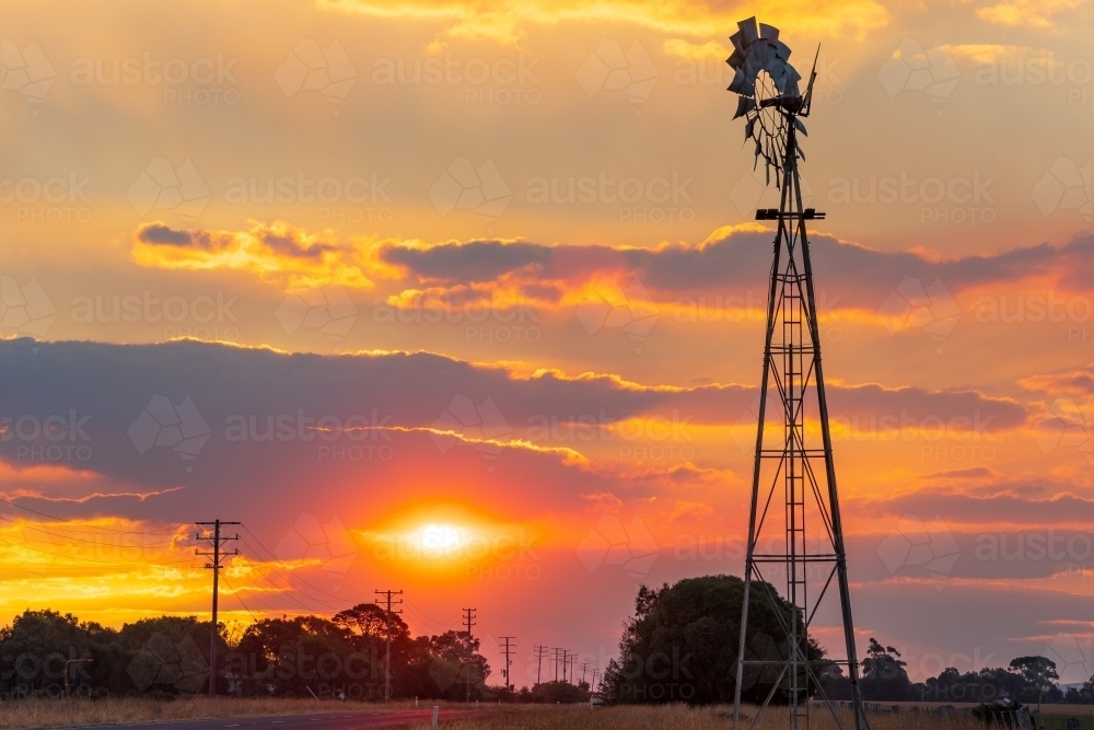Silhouette of a farm windmill against a smokey sunset sky - Australian Stock Image