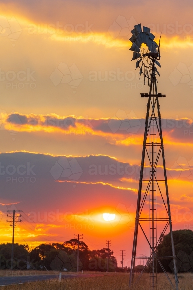Silhouette of a farm windmill against a smokey sunset sky - Australian Stock Image