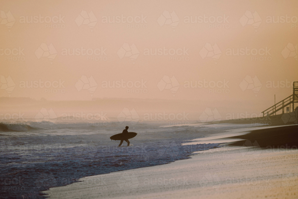 Silhouette of a lone surfer getting off the beach with his board - Australian Stock Image