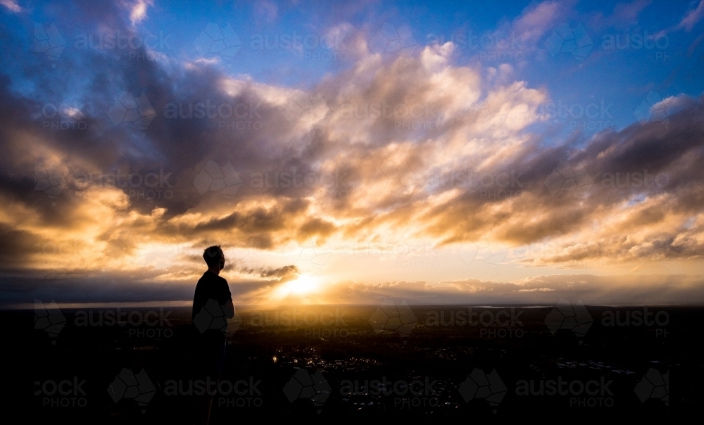 Silhouette of a man standing alone looking out at sunset - Australian Stock Image