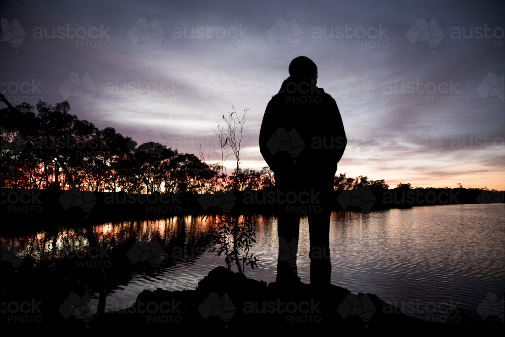 Silhouette of a person looking over water before sunrise - Australian Stock Image