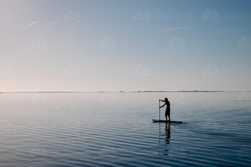 Silhouette of a person on a stand-up paddle board of calm water - Australian Stock Image