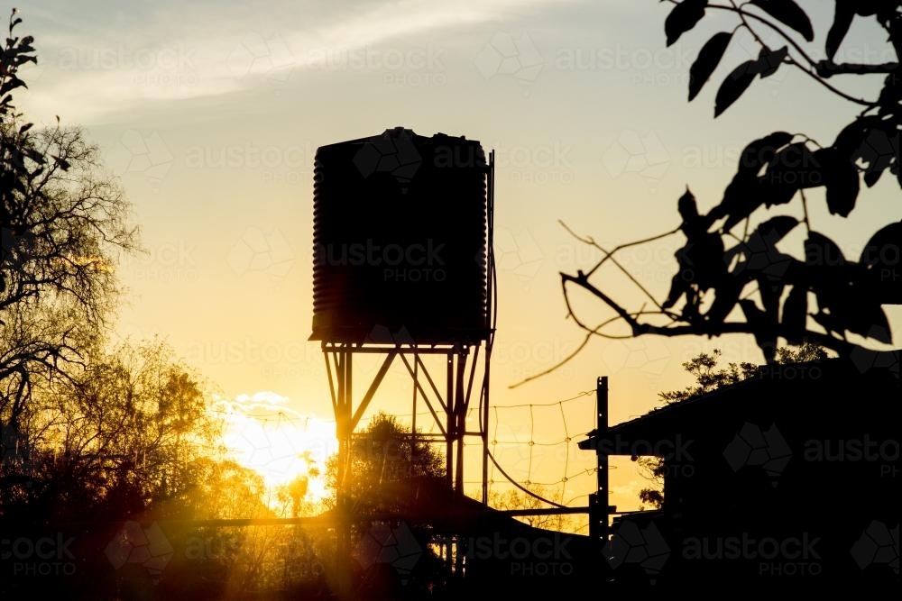 Silhouette of a rain water tank on a stand at sunset - Australian Stock Image