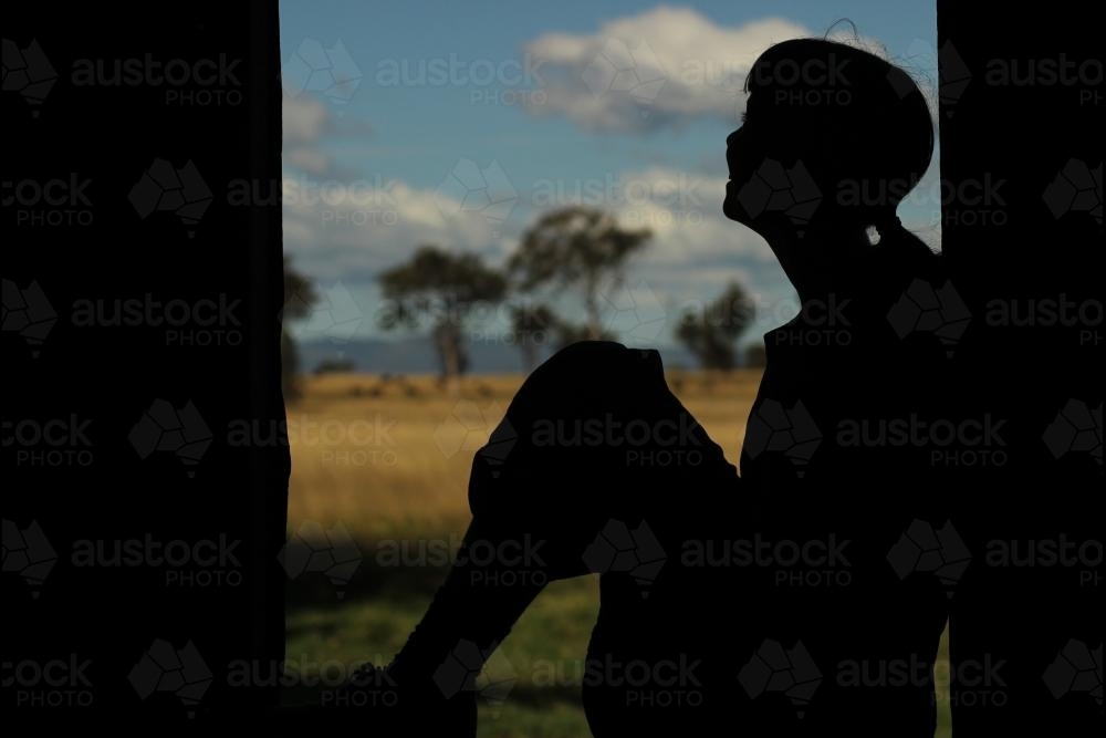 Silhouette of a young girl sitting in a window frame - Australian Stock Image