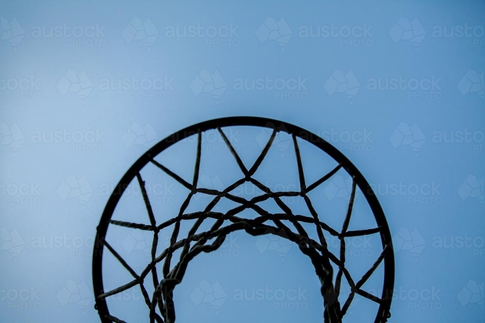 Silhouette of basketball hoop and net against blue sky - Australian Stock Image