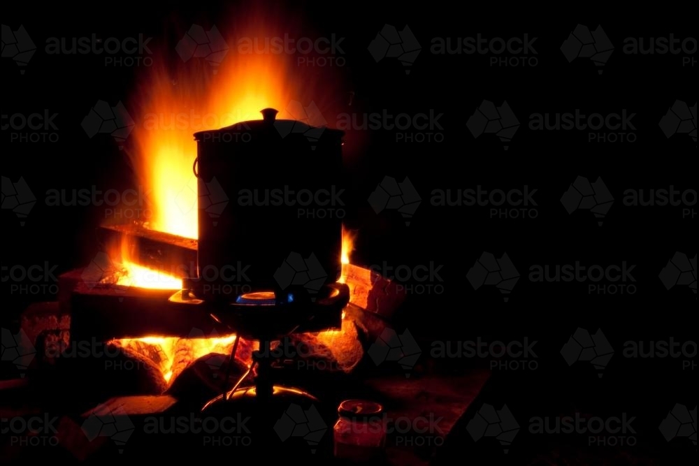 Silhouette of billy can sitting on a fire at night - Australian Stock Image