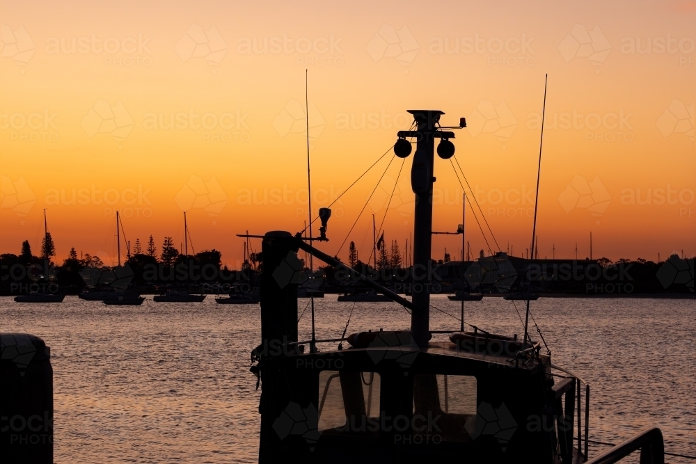 Silhouette of boat at sunset with marina in background - Australian Stock Image
