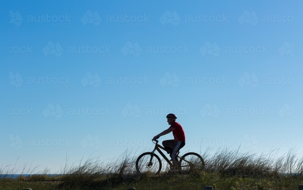 Silhouette of boy on bike with coastal grass - Australian Stock Image