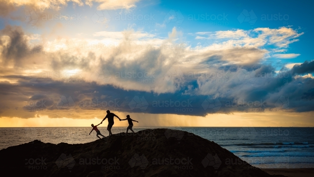 Silhouette of father and sons walking together holding hands on sand dune - Australian Stock Image