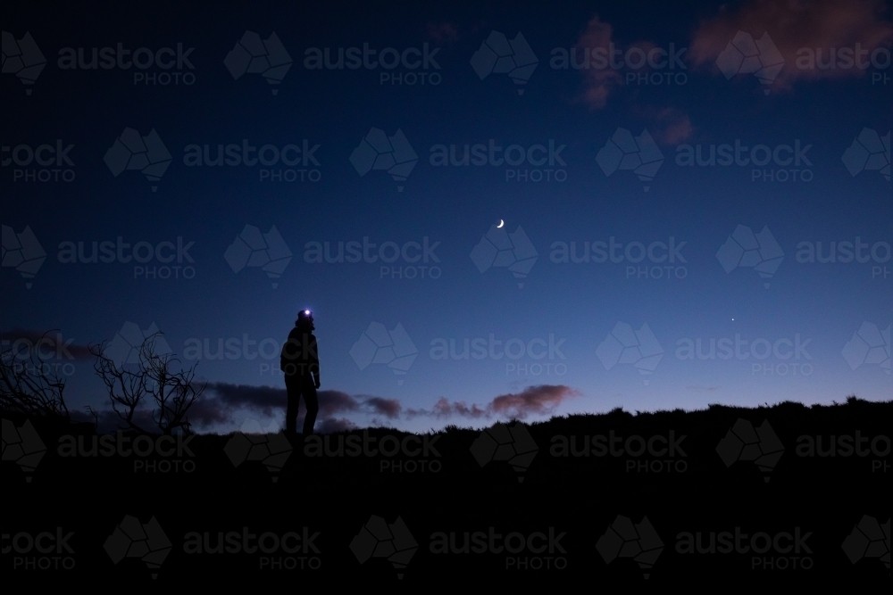 Silhouette of female standing with moon behind at dawn - Australian Stock Image