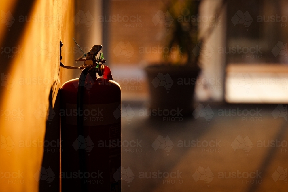 Silhouette of fire extinguisher in motel hallway illuminated by golden afternoon sunlight - Australian Stock Image