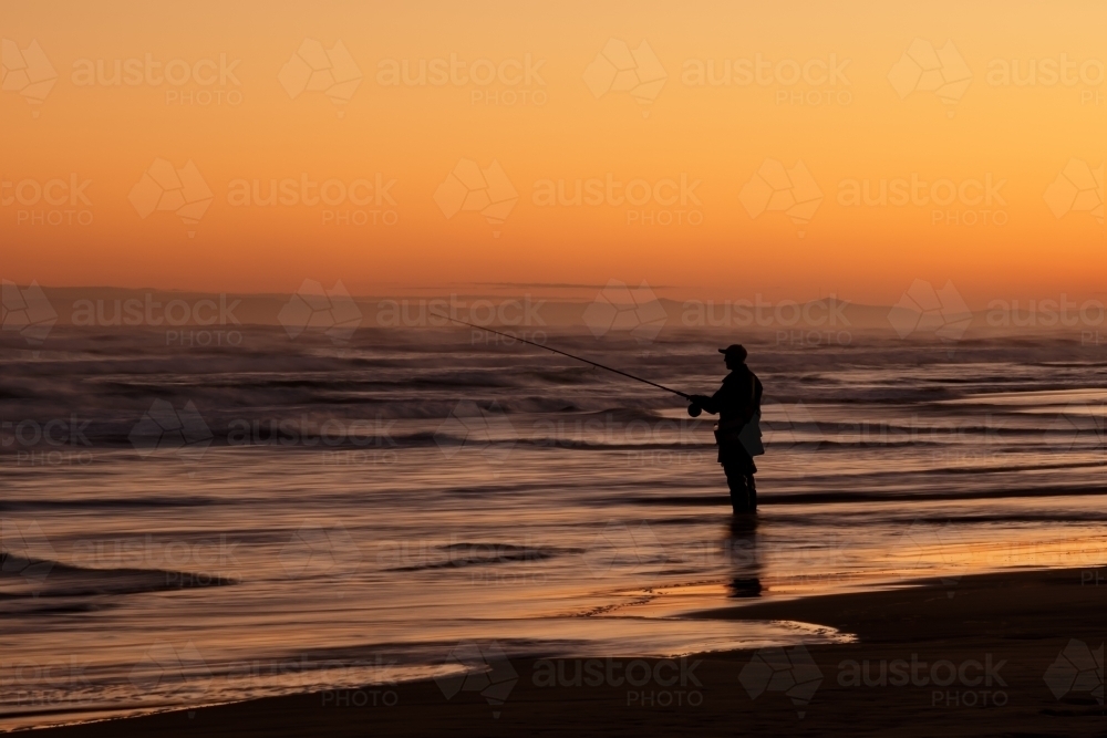 Silhouette of fisherman standing in shallow water at sunset - Australian Stock Image