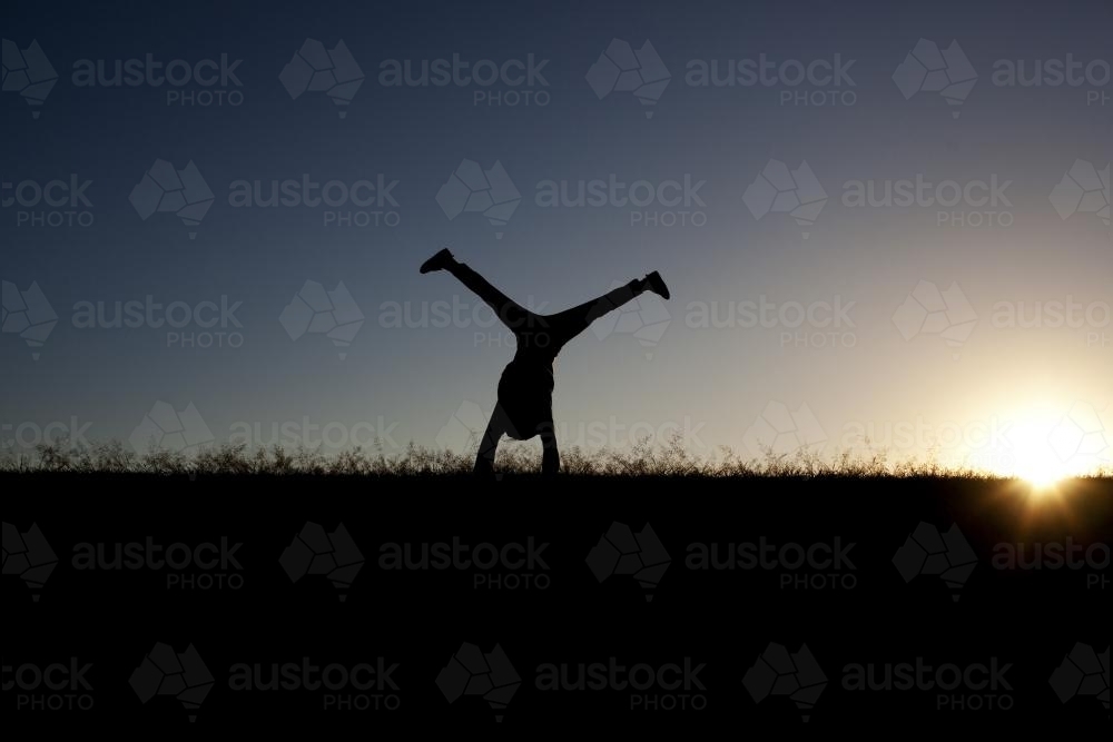 Silhouette of girl doing a cartwheel at sunset - Australian Stock Image