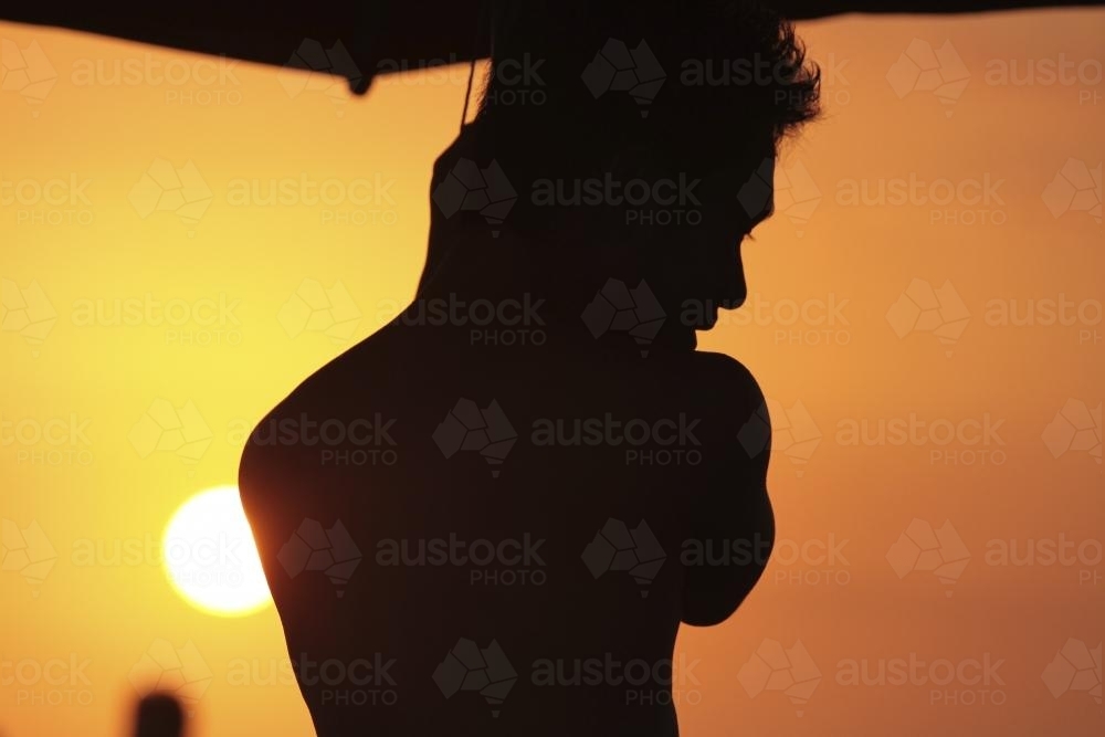 Silhouette of man against orange sky at beach - Australian Stock Image