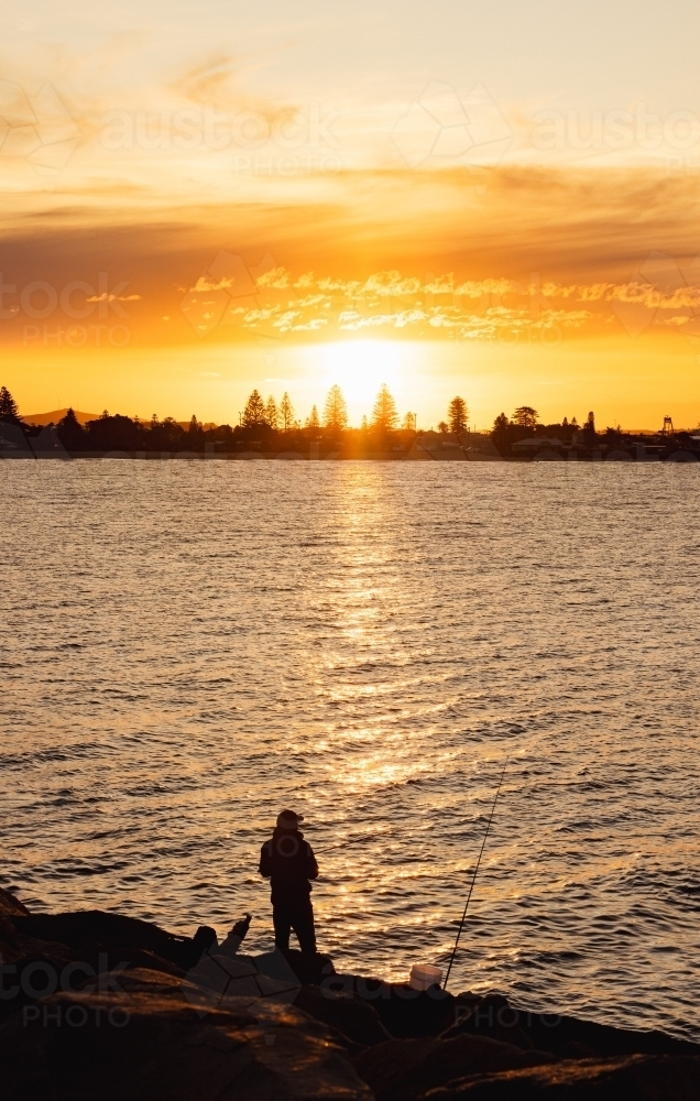 Silhouette of man fishing at sunset from the breakwall at Stockton, NSW - Australian Stock Image