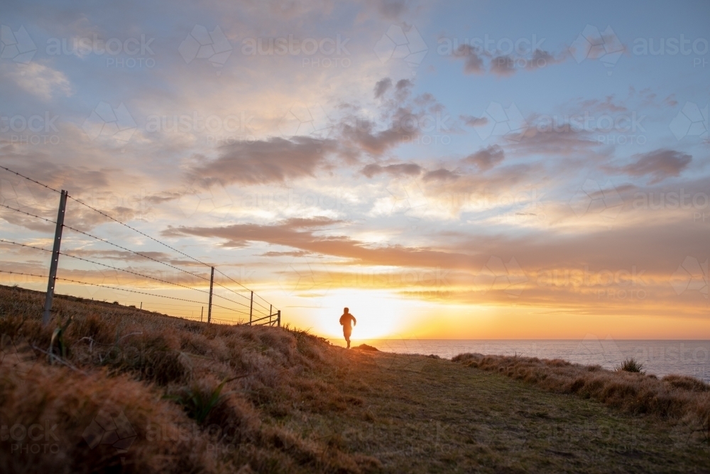 Silhouette of Man in Distance Running Towards Sunrise - Australian Stock Image