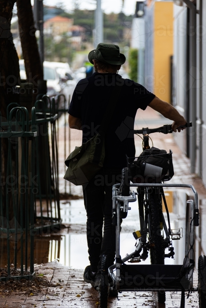 silhouette of man pushing bike down wet alley - Australian Stock Image