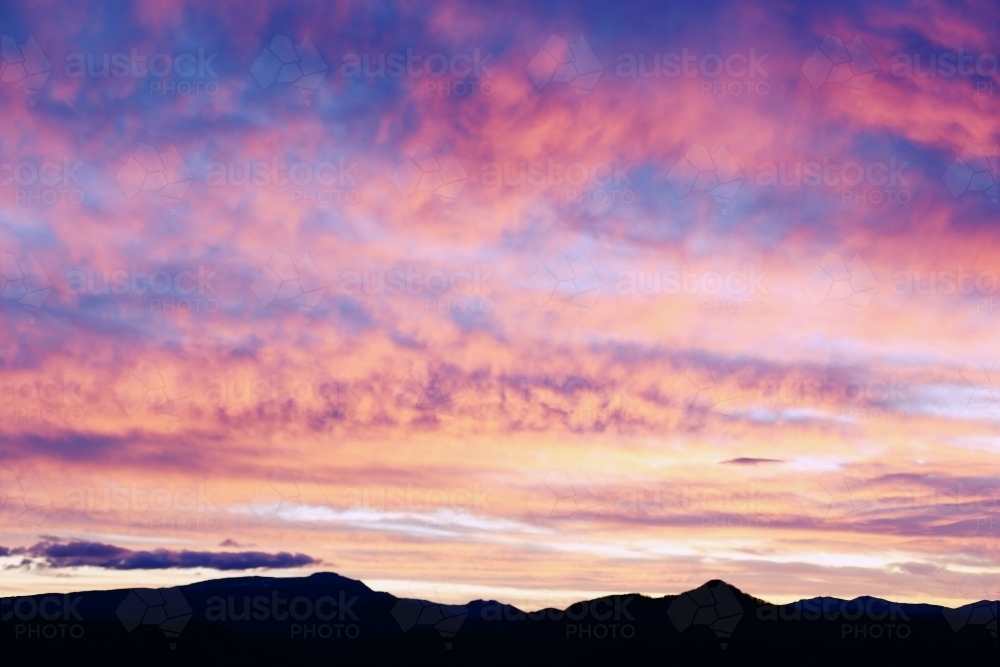 Silhouette of mountains under a dramatic sky at sunset. - Australian Stock Image
