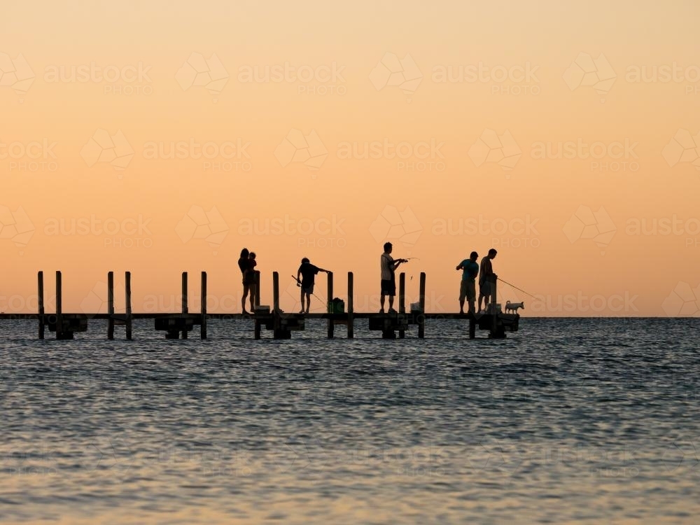 Silhouette of people fishing off a jetty at dusk - Australian Stock Image