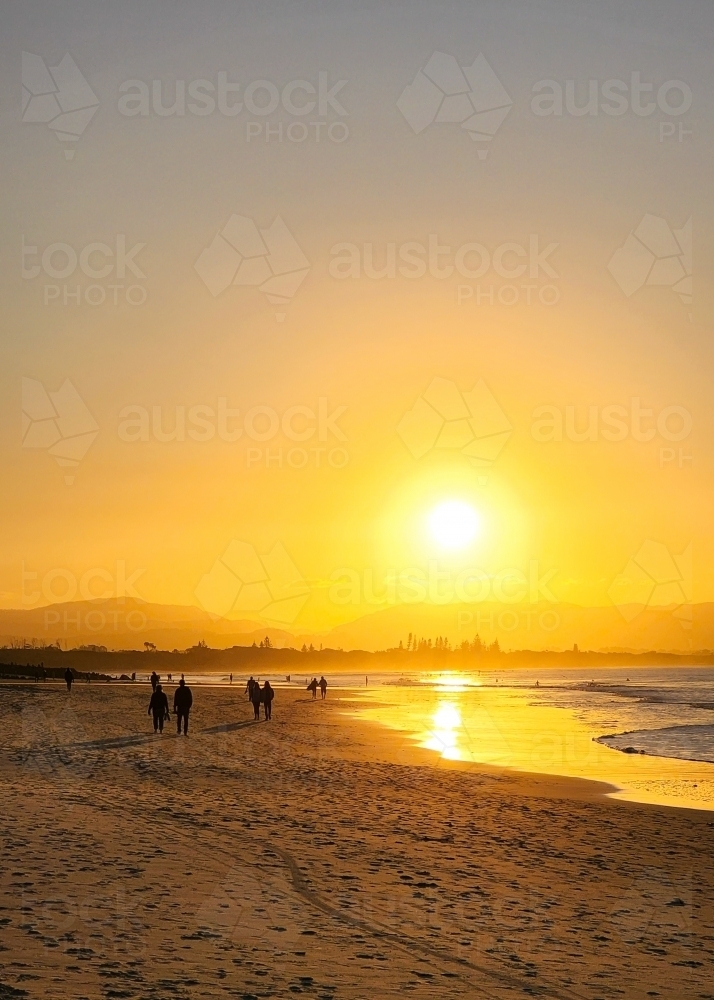 Silhouette of people walking on the beach at Byron Bay at sunset - Australian Stock Image