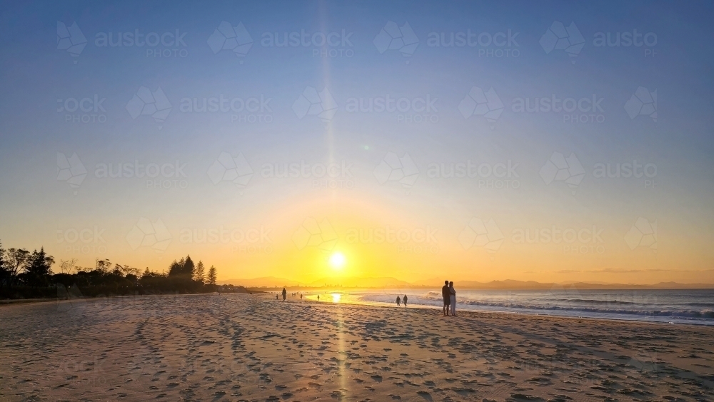 Silhouette of people walking on the beach at Byron Bay at sunset - Australian Stock Image