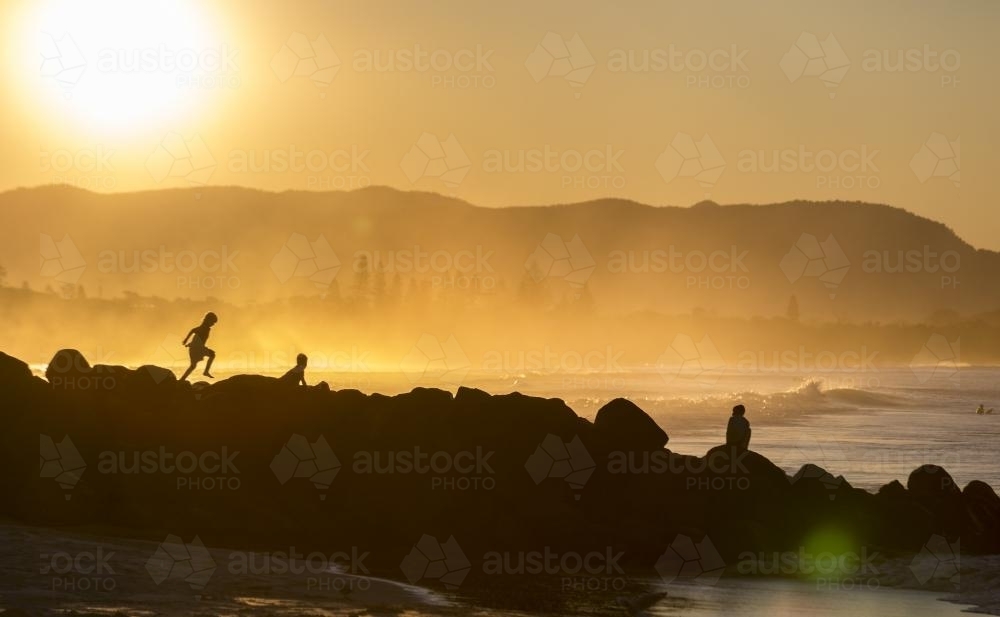 Silhouette of people walking over rocks near the ocean - Australian Stock Image