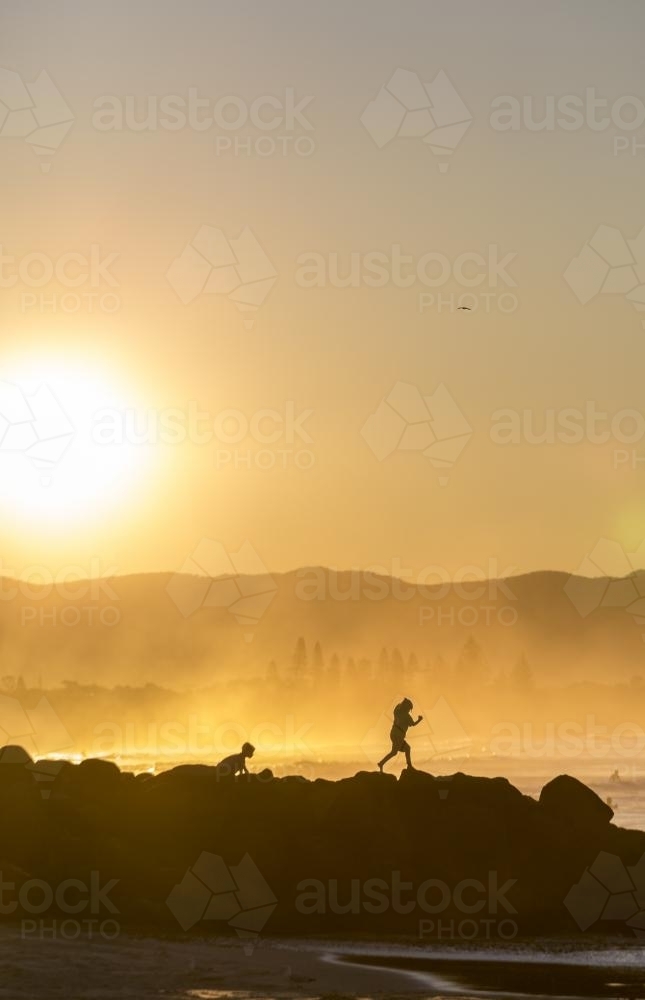 Silhouette of people walking over rocks near the ocean - Australian Stock Image
