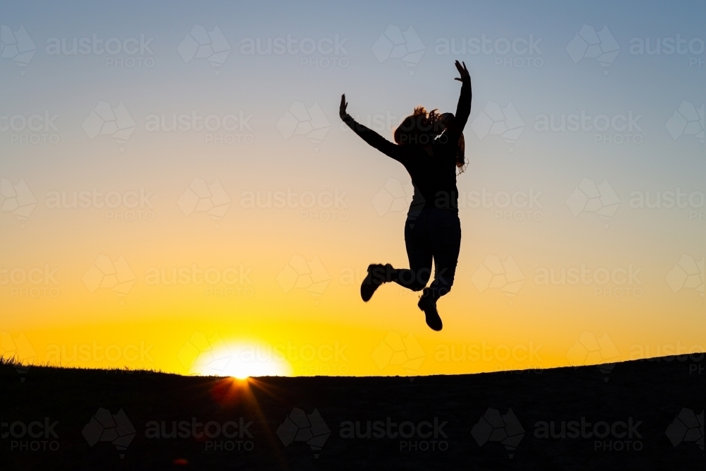 Silhouette of person jumping for joy at sunset - Australian Stock Image