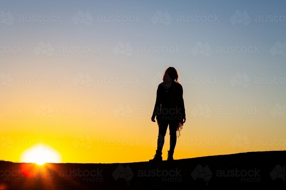 Silhouette of person standing against a glowing sunset - Australian Stock Image