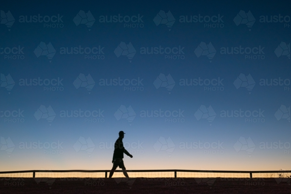 Silhouette of person walking along walkway at dawn. - Australian Stock Image