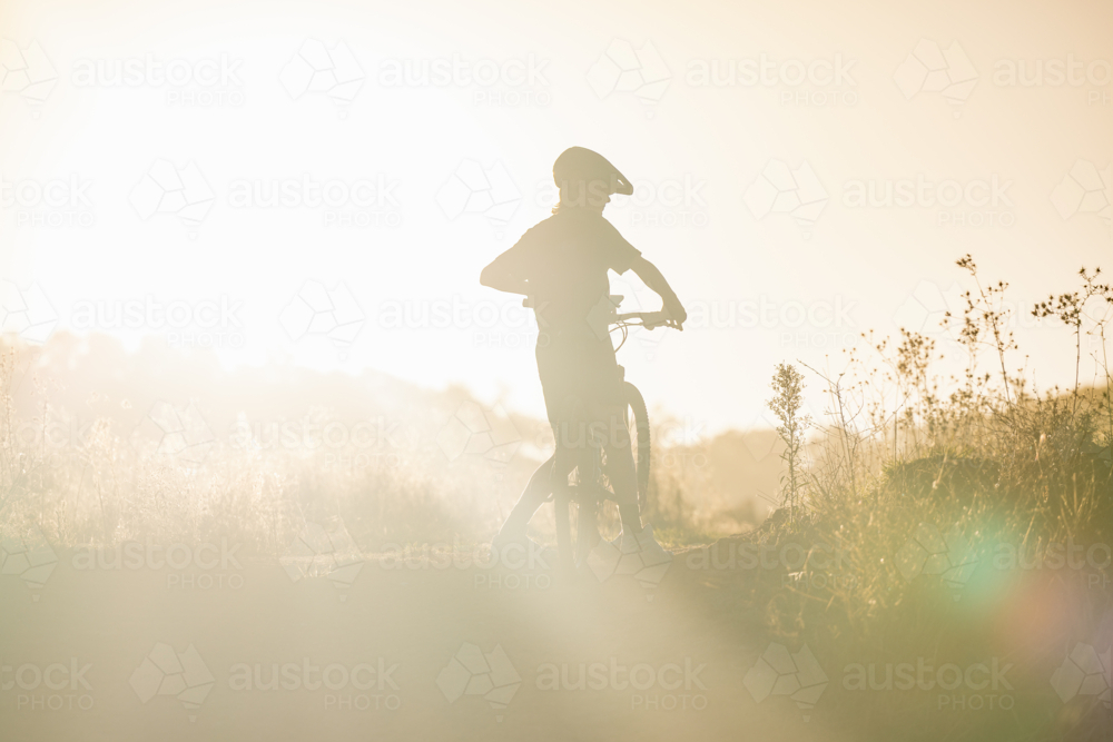 Silhouette of teenage boy on rural dirt road bathed in vibrant afternoon light - Australian Stock Image