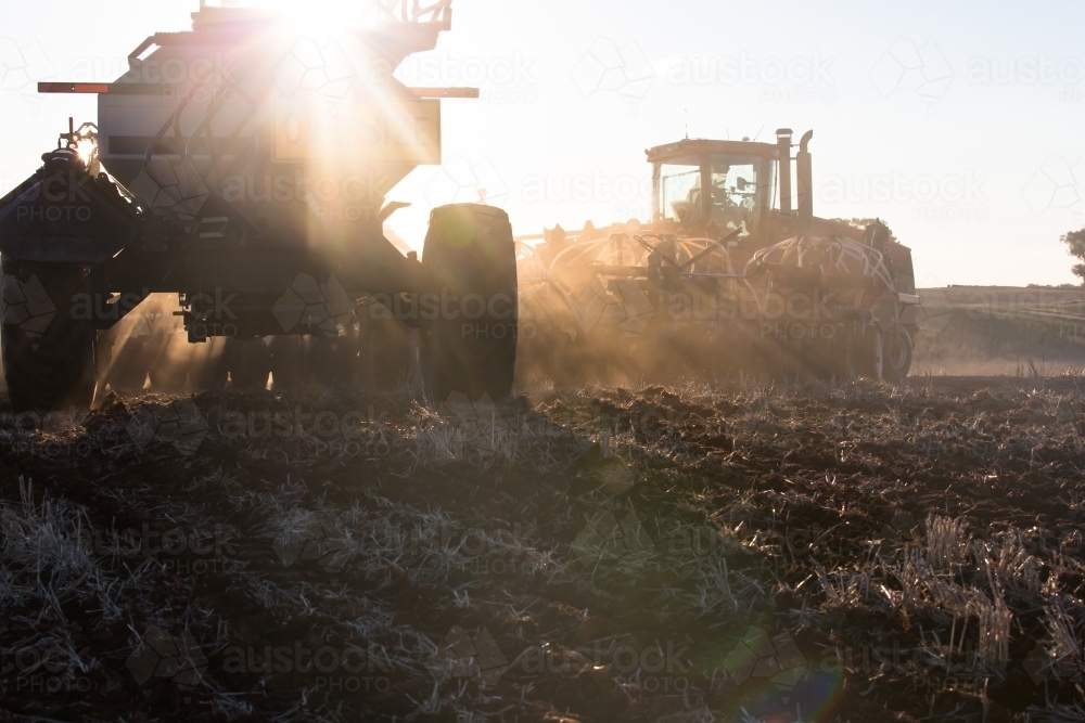 Silhouette of tractors ploughing soil at dusk in paddock - Australian Stock Image