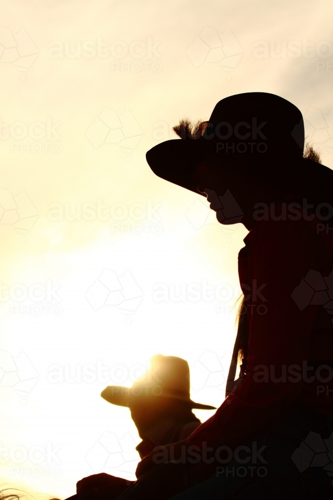 Silhouette of two country girls in their twenties, as they ride their horses - Australian Stock Image