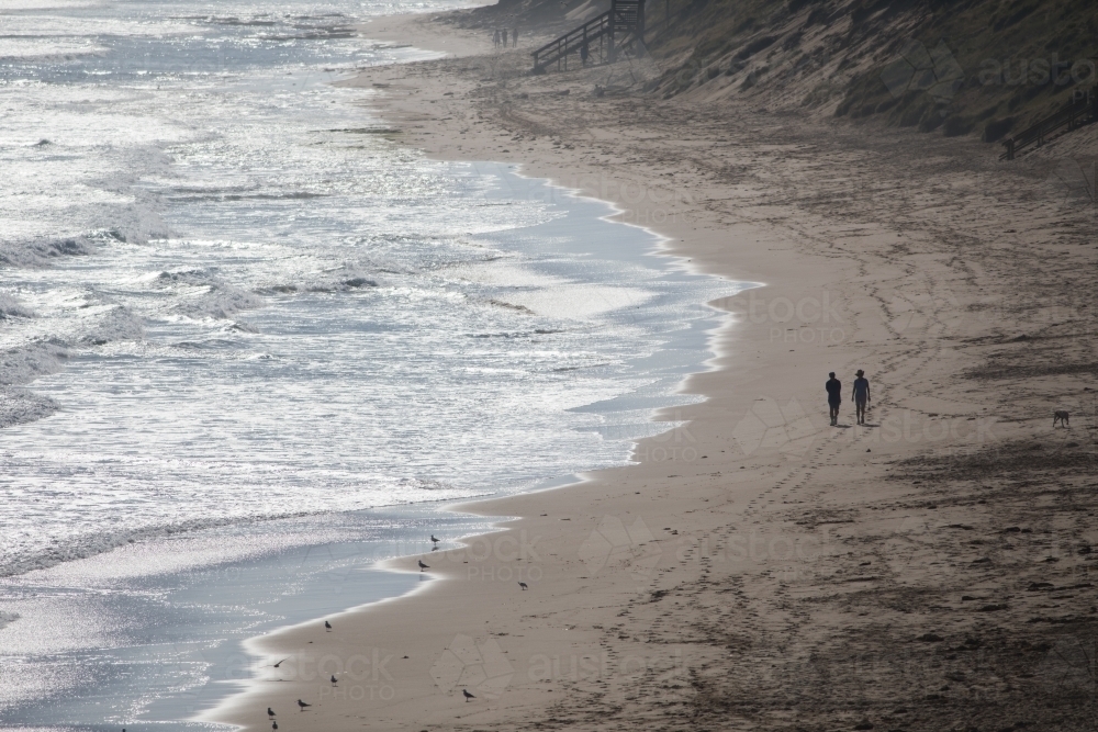Silhouette of two distant people walking along a beach - Australian Stock Image