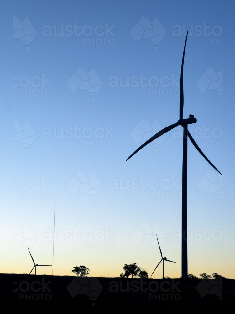 silhouette of wind turbines, trees and meteorological mast against darkening blue sky at dusk - Australian Stock Image