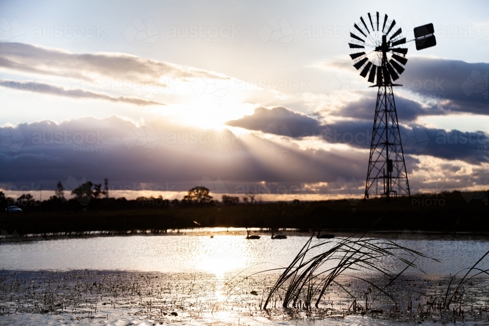 Silhouette of windmill and sunlight and farm dam at sunset - Australian Stock Image