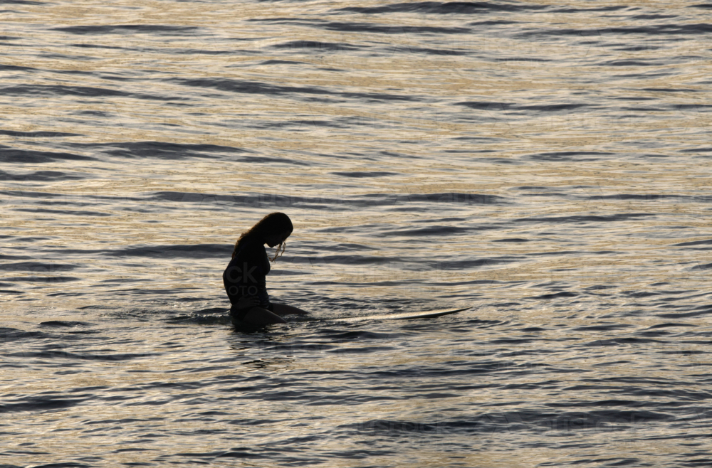 silhouette of woman on surfboard in golden sunset water - Australian Stock Image