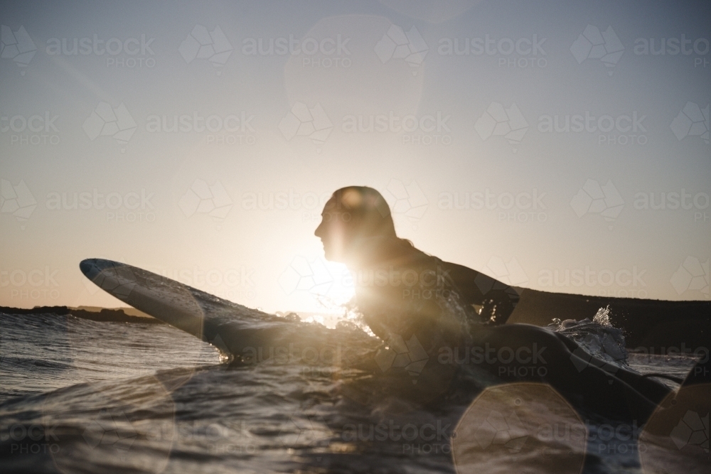 Silhouette of woman surfing at sunset - Australian Stock Image
