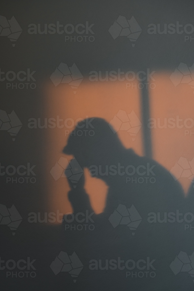 Silhouette shadow of a man with his head in his hands looking depressed - Australian Stock Image