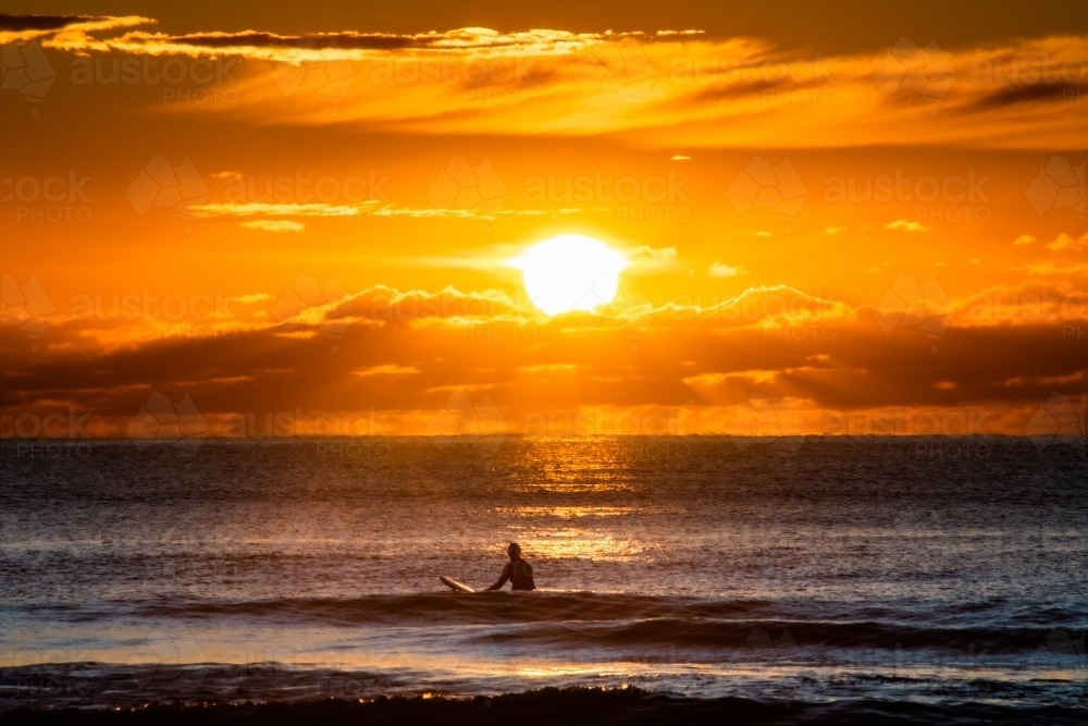 silhouette shot of a man surfing at the beach during sunset/sunrise with orange skies - Australian Stock Image