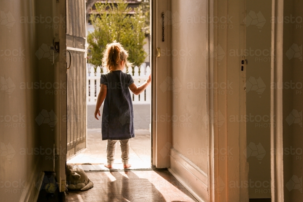 silhouette shot of the back of a girl wearing blue dress and grey pants standing in the corridor - Australian Stock Image