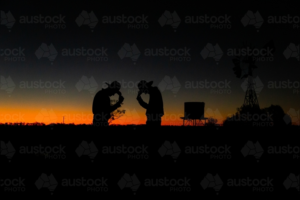 Silhouette shot of two men wearing hats looking down during sunset - Australian Stock Image