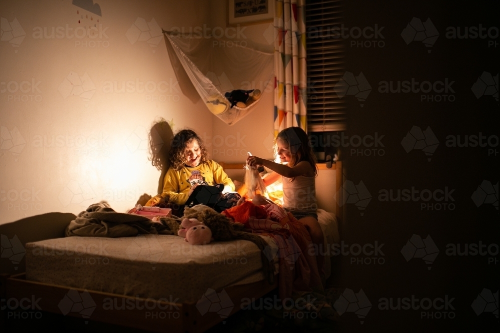 Silhouette shot of two smiling girls playing in the dark room on the bed - Australian Stock Image